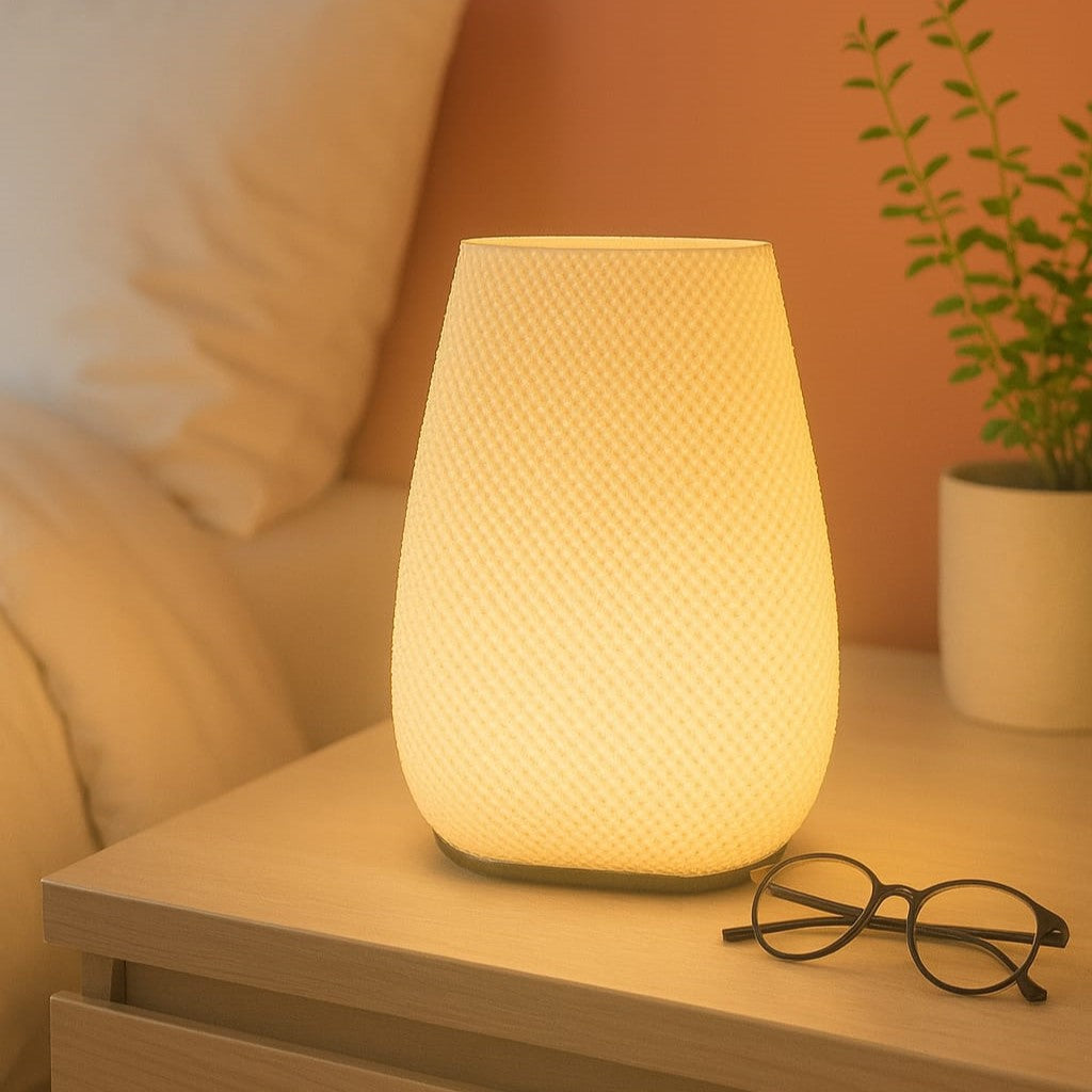 Soft glowing bedside lamp on nightstand beside glasses and plant — warm ambient bedroom lighting for modern interiors.