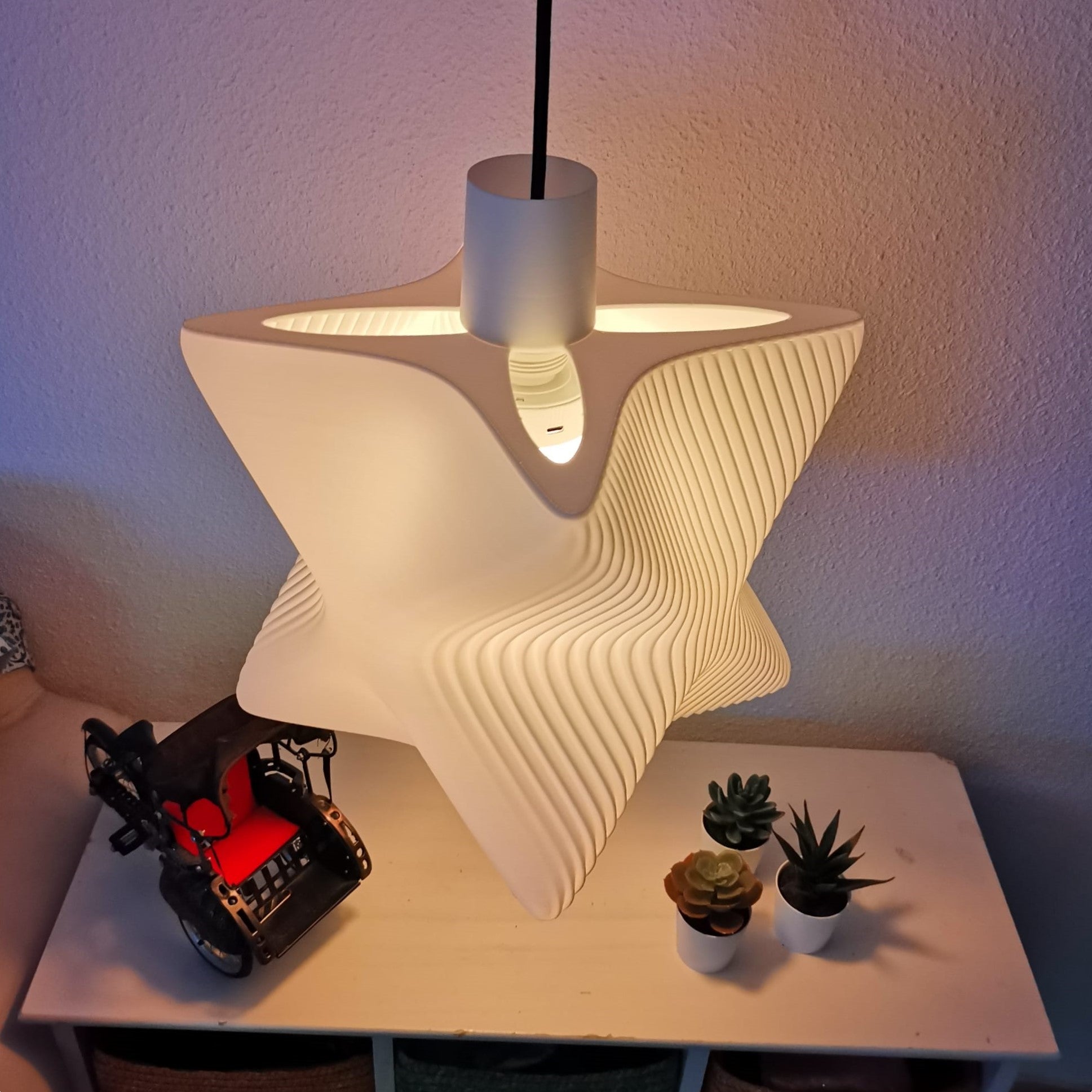 Star-shaped lamp on a table with small plants and a toy car.