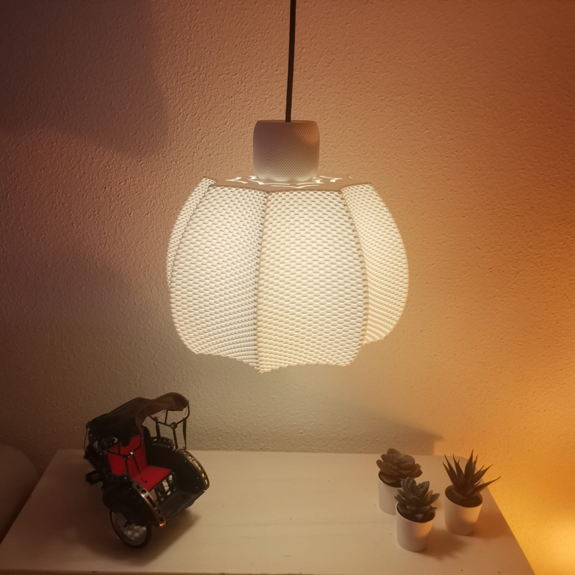 Textured pendant light fixture casting a warm glow on a wall with decorative items below.