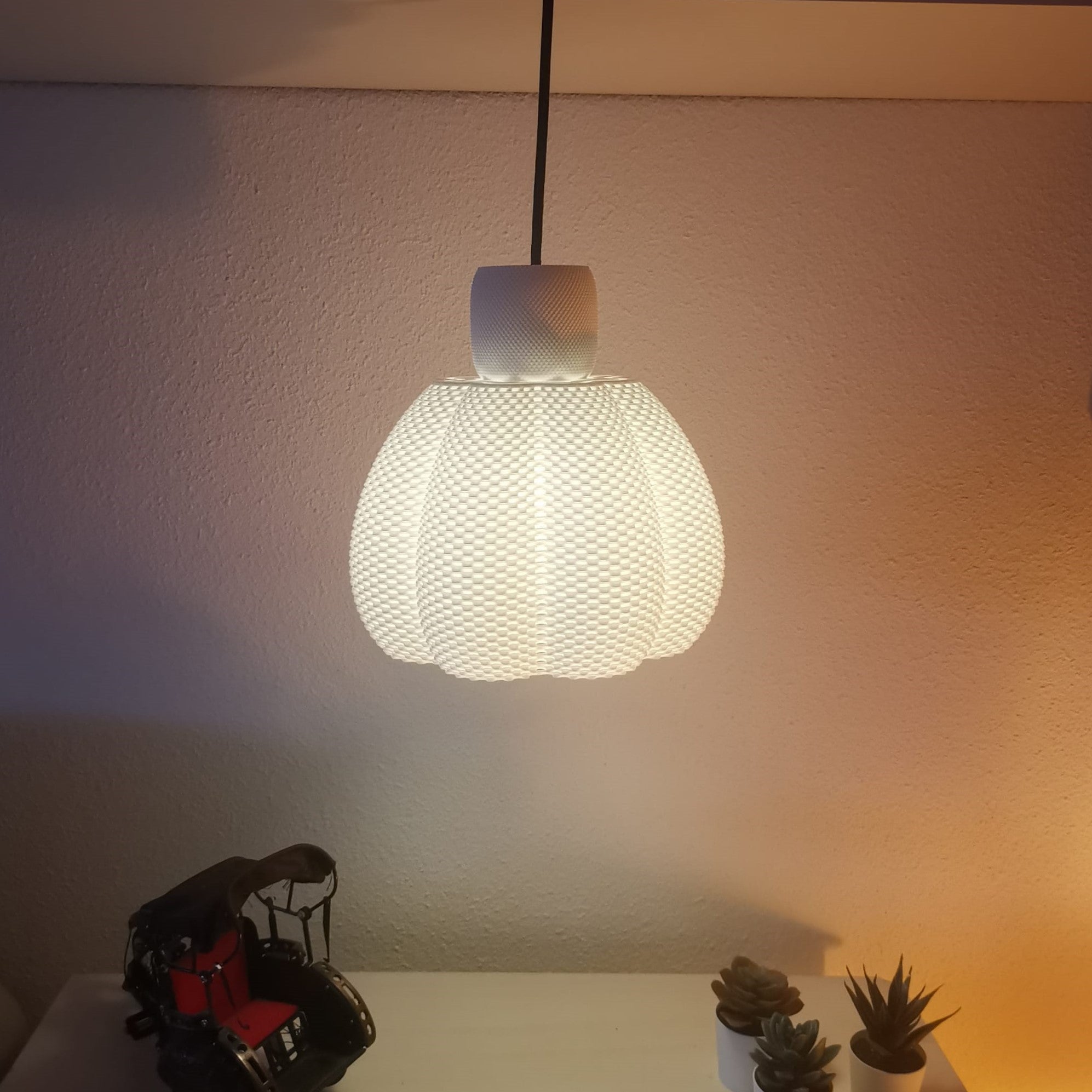 Textured pendant light fixture on a neutral wall with decorative items below.