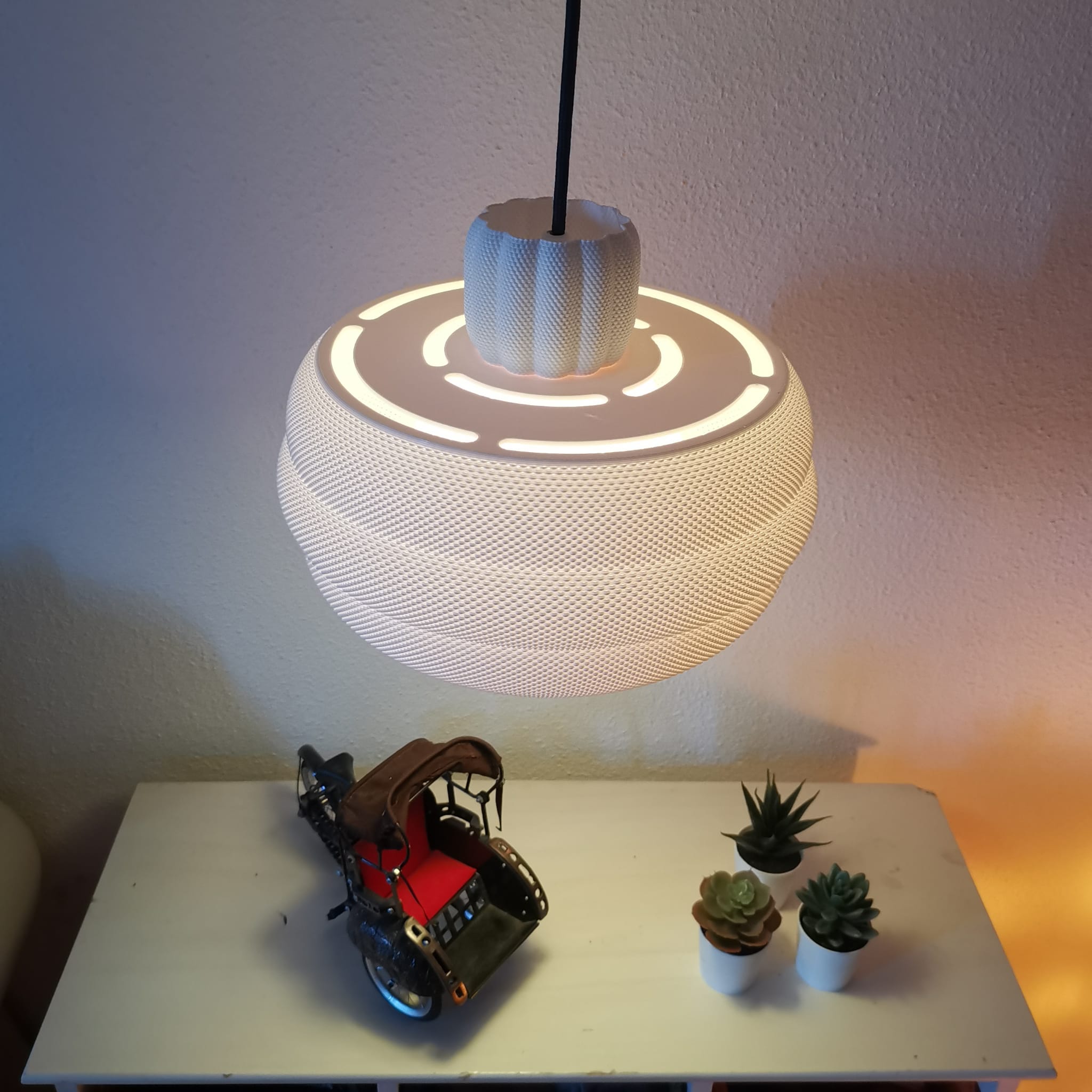 Spherical lamp with a textured design on a table with small plants and a model car.