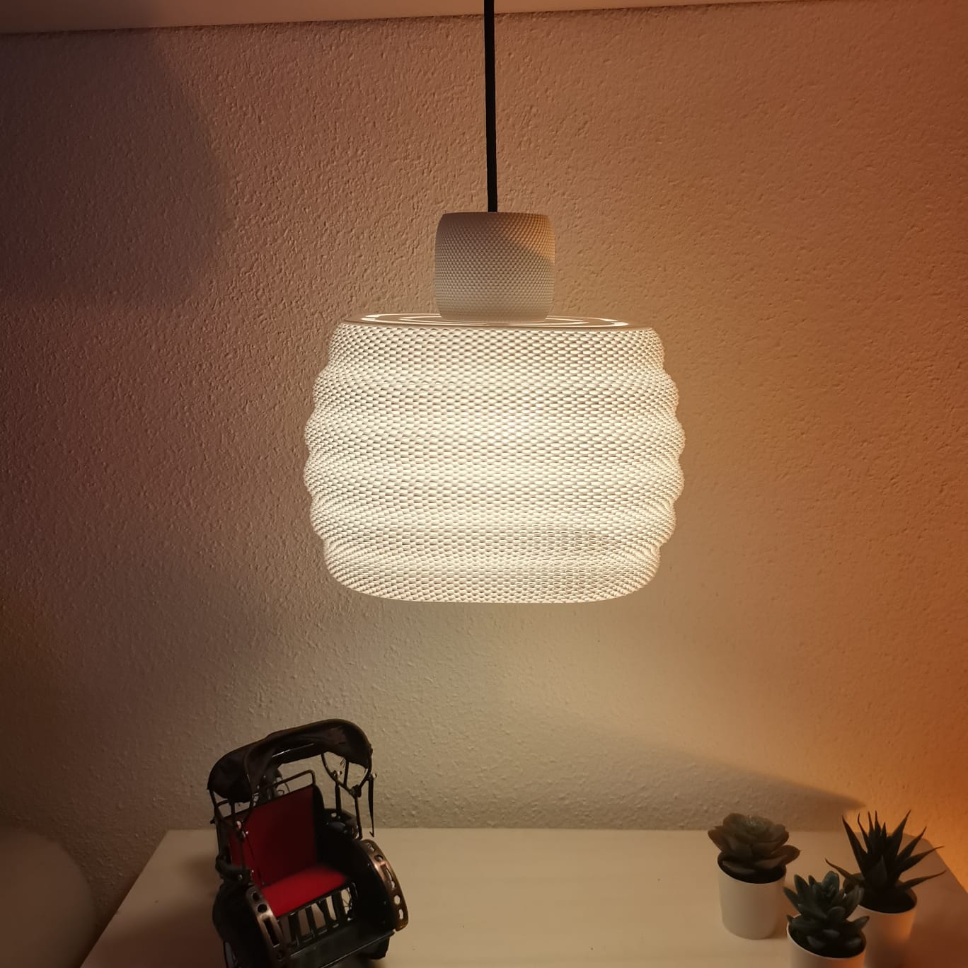 Textured pendant light hanging above a table with decorative items against a plain wall.