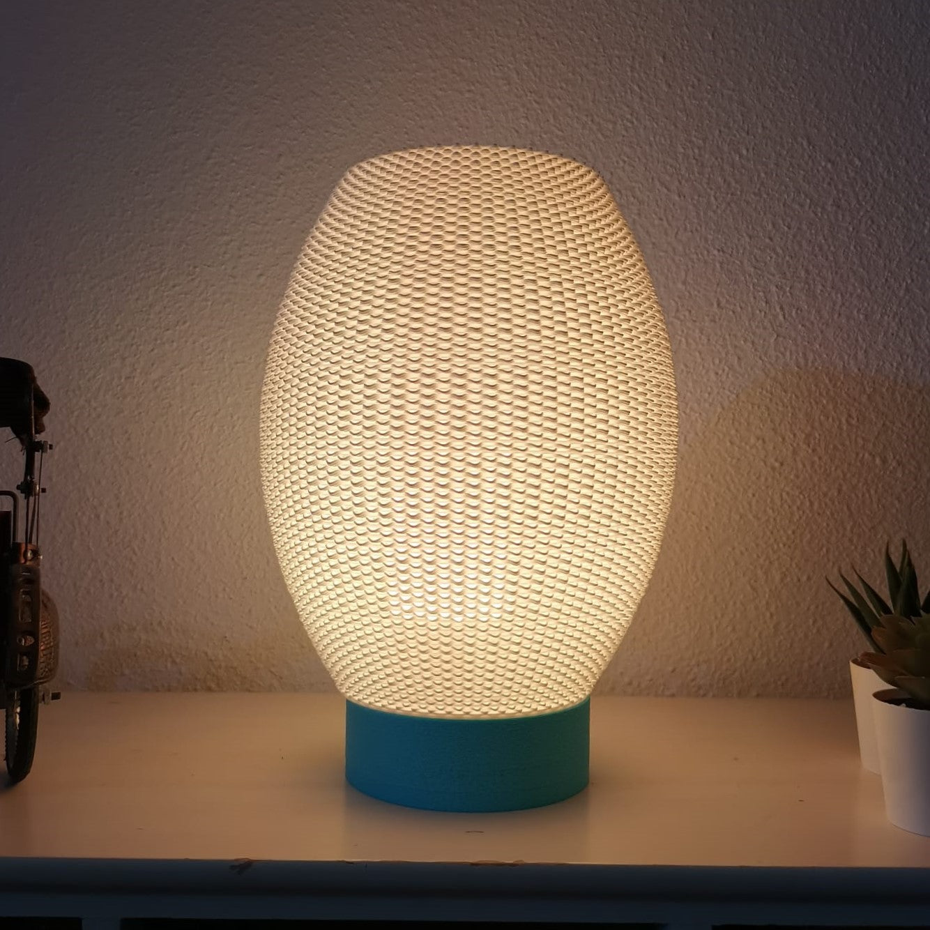 Textured table lamp with a blue base on a surface against a neutral wall.