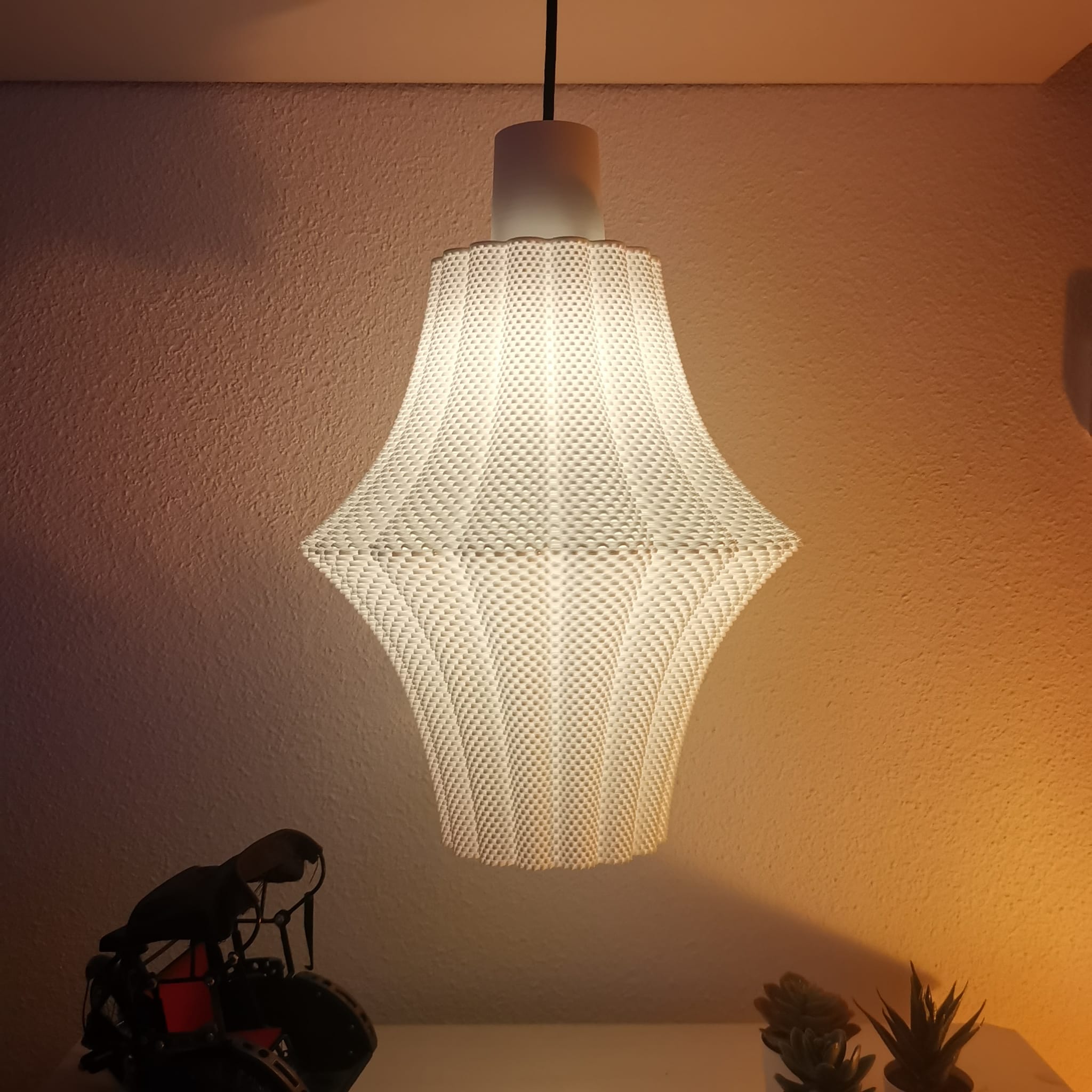 Textured pendant light hanging against a neutral wall with a warm glow.