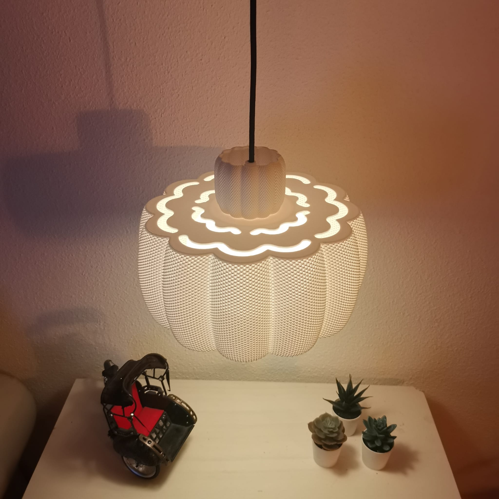 Decorative lamp with a wavy design on a table with small plants and a model car.