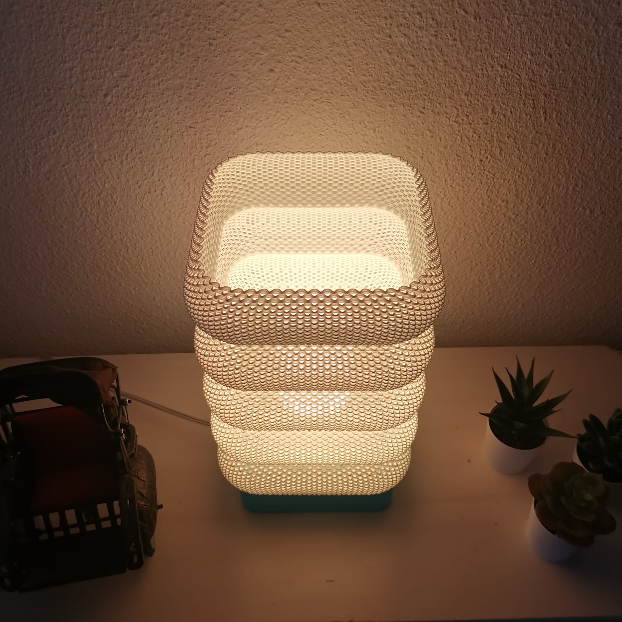 Decorative lamp with textured design on a surface with plants and a basket.