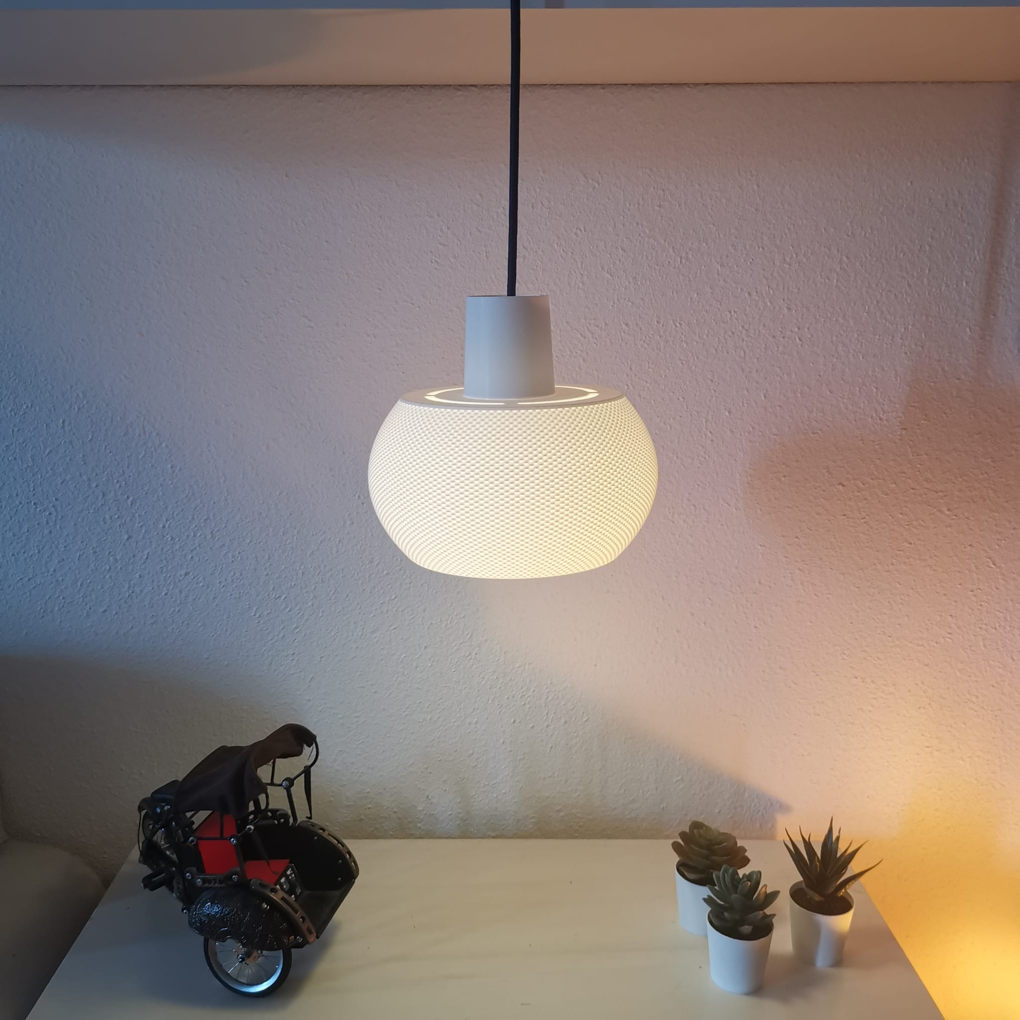 Modern pendant light hanging above a table with decorative items against a plain wall.