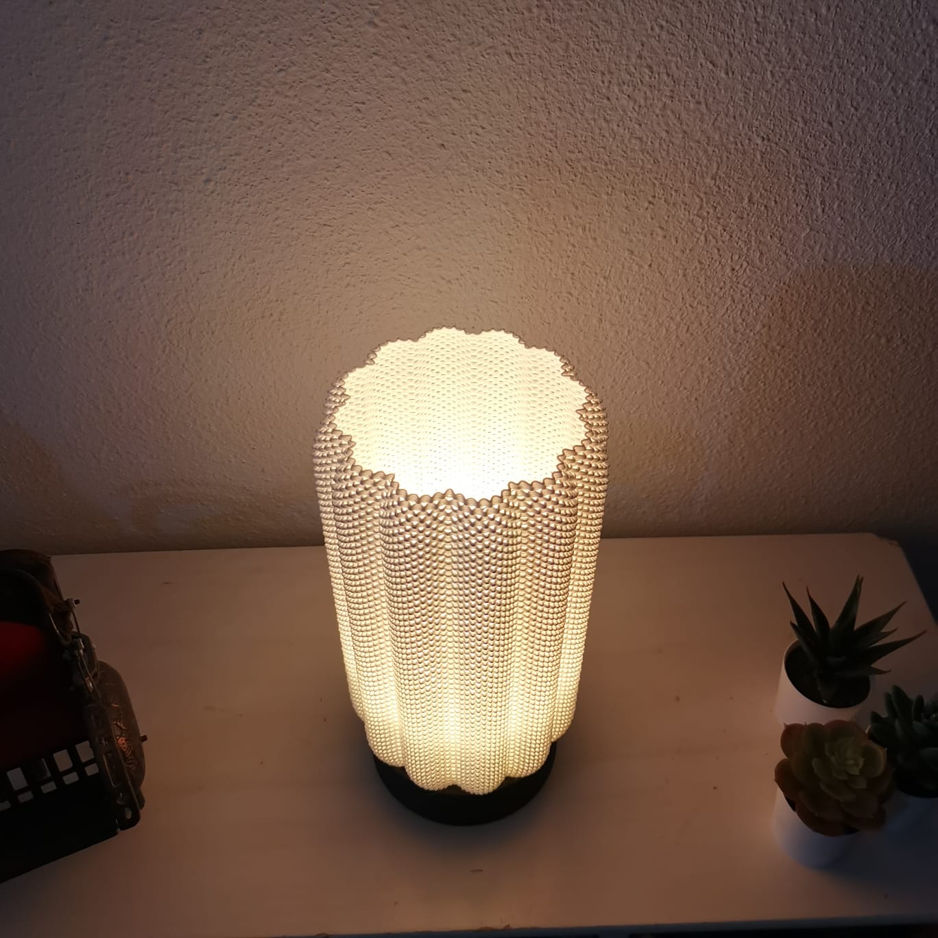 Decorative lamp with a textured design on a table against a plain wall.