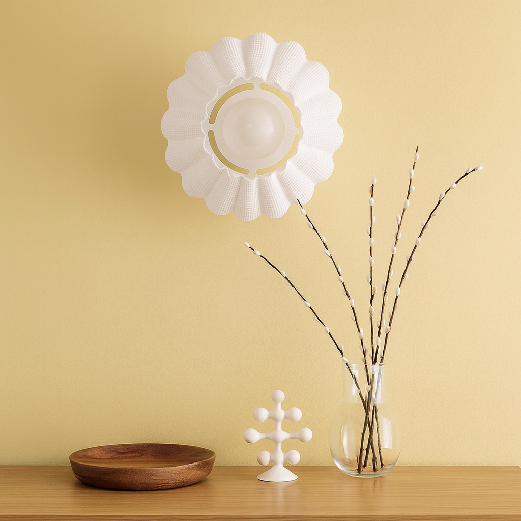 Decorative wall art with a white flower shape on a yellow wall, accompanied by a wooden bowl, glass vase with branches, and small white sculpture.