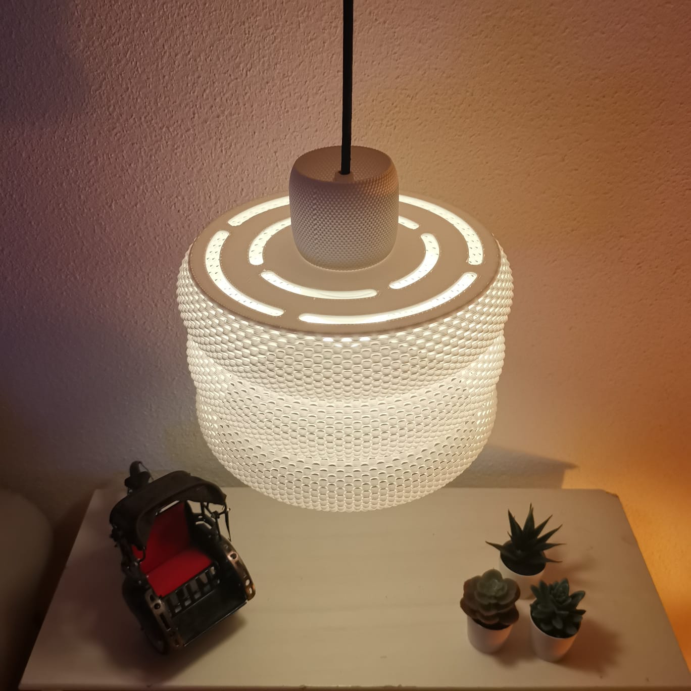Textured pendant light on a table with small plants and a toy car.