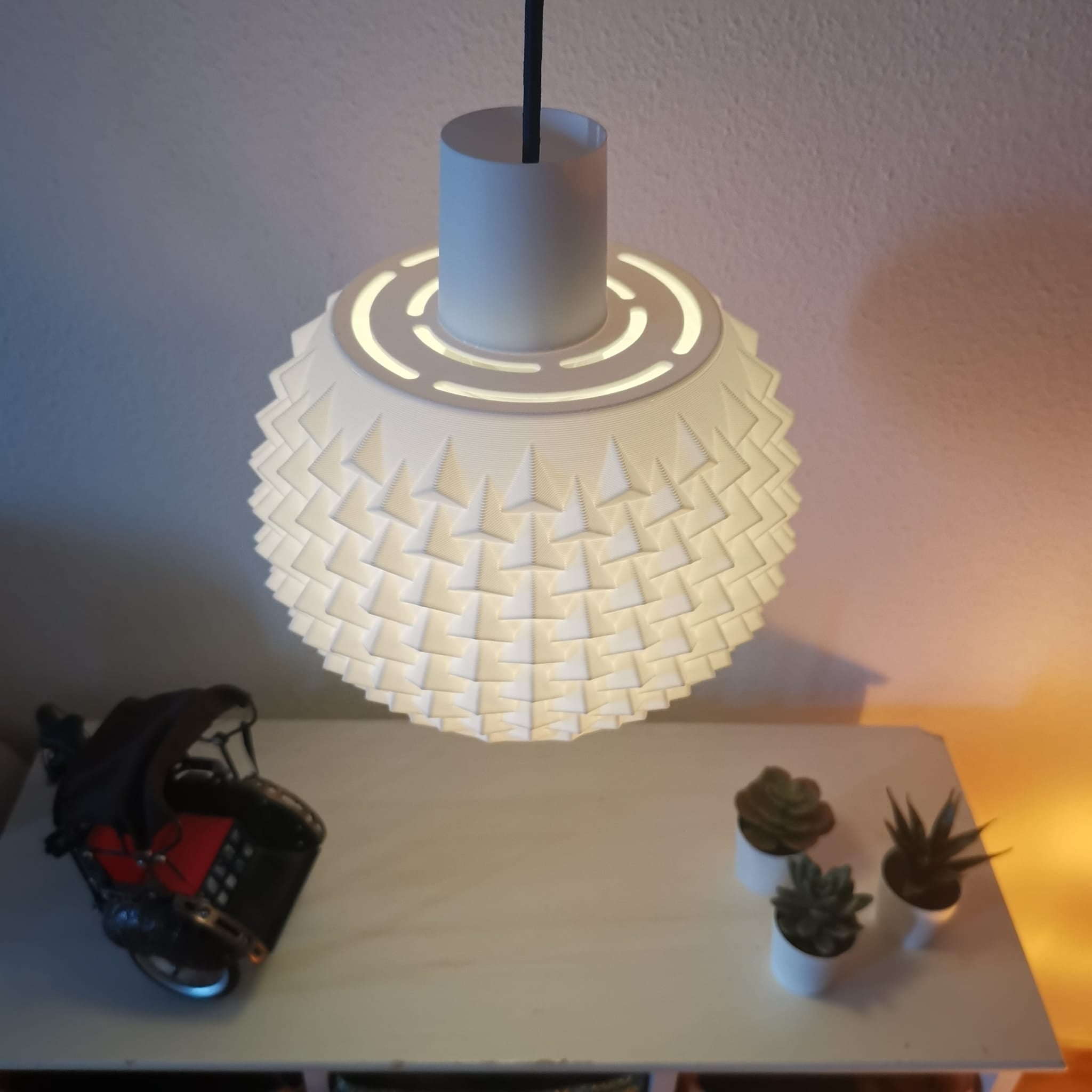 White textured pendant light on a table with a toy and plants