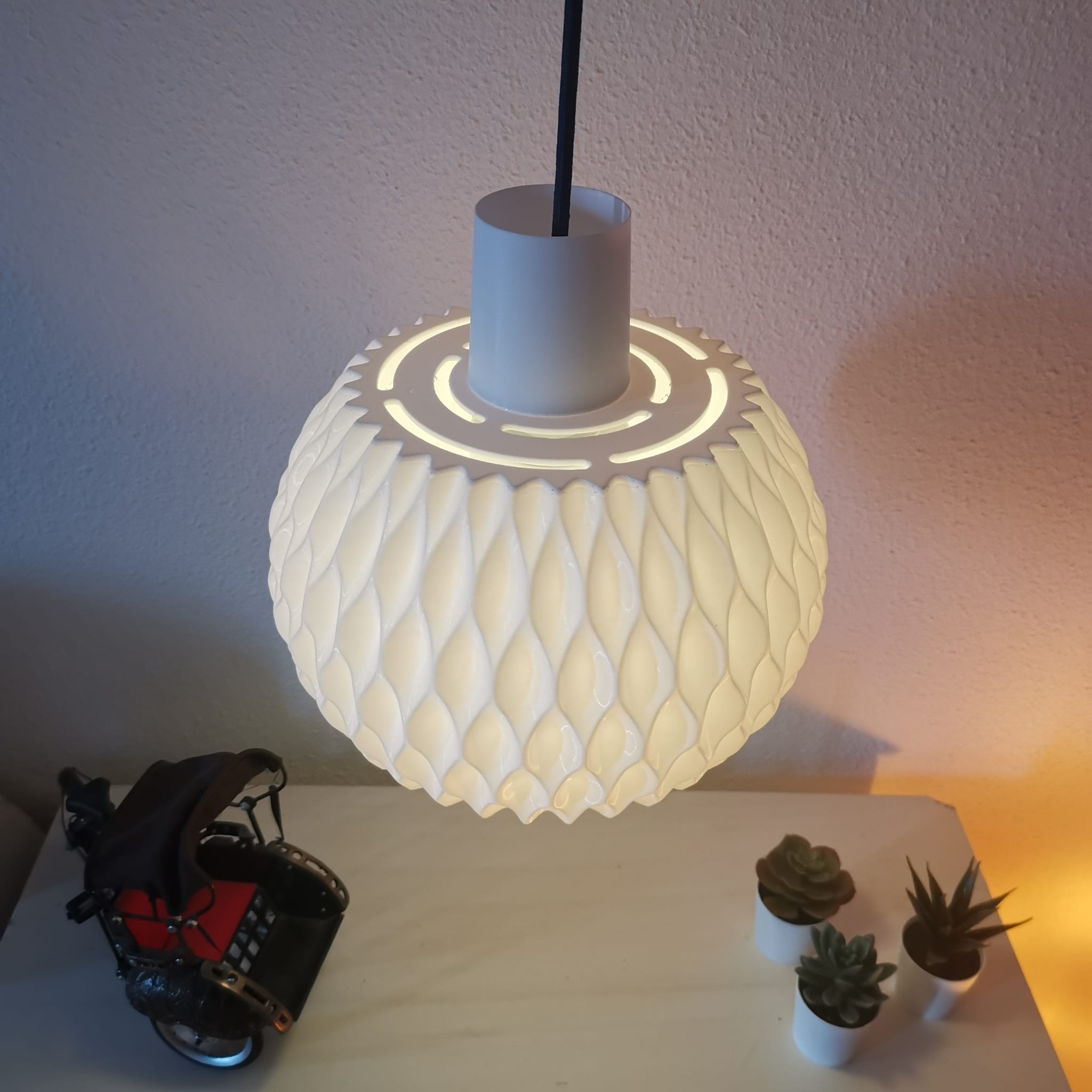 Decorative lamp with a textured design on a white surface with small plants and a model car.