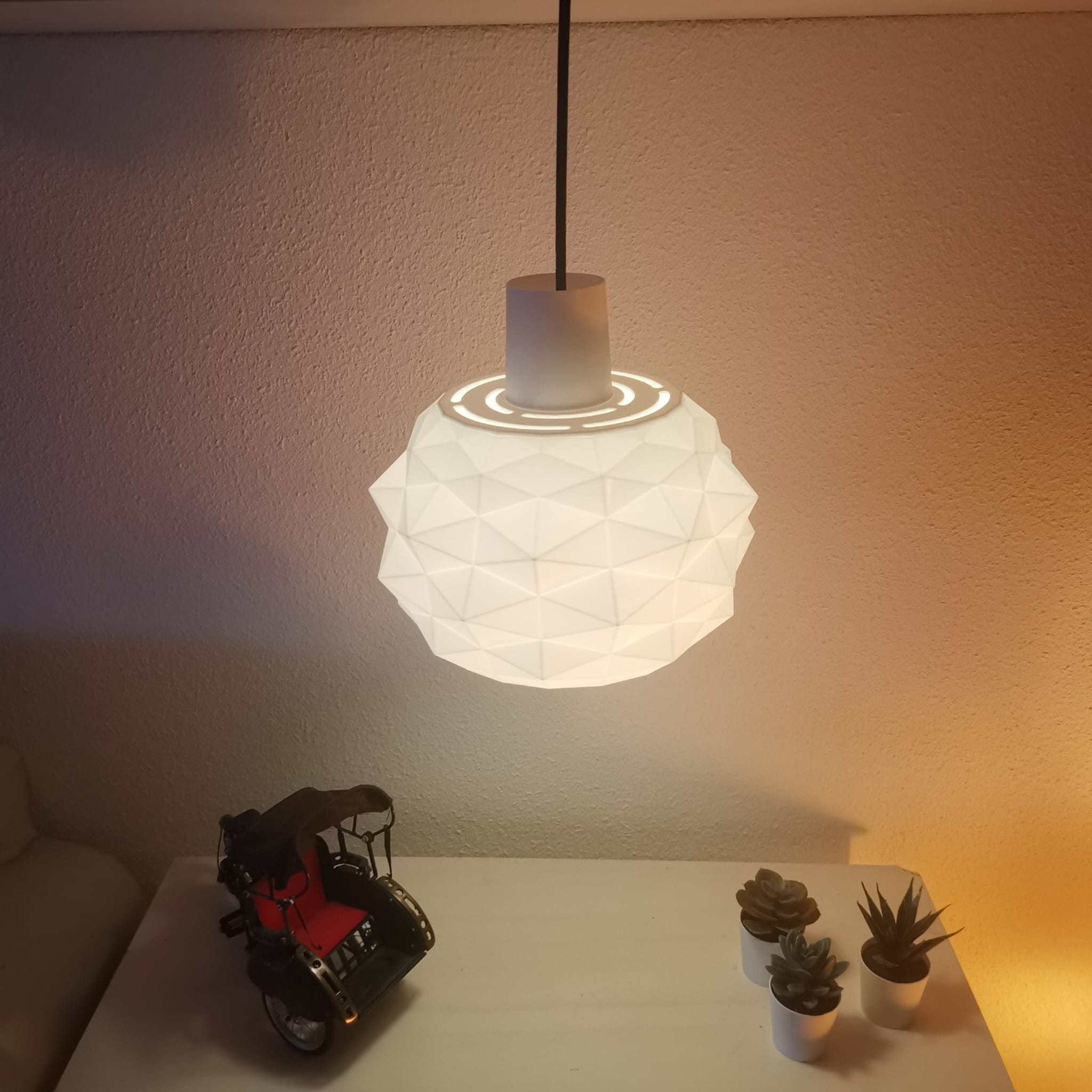 Modern pendant light fixture on a table with decorative items against a neutral wall.
