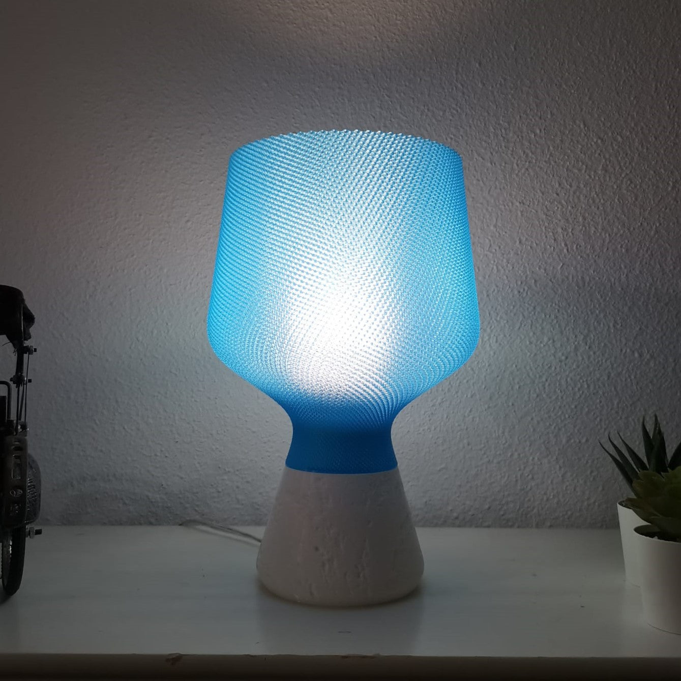 Blue textured table lamp on a white surface with a light gray wall background