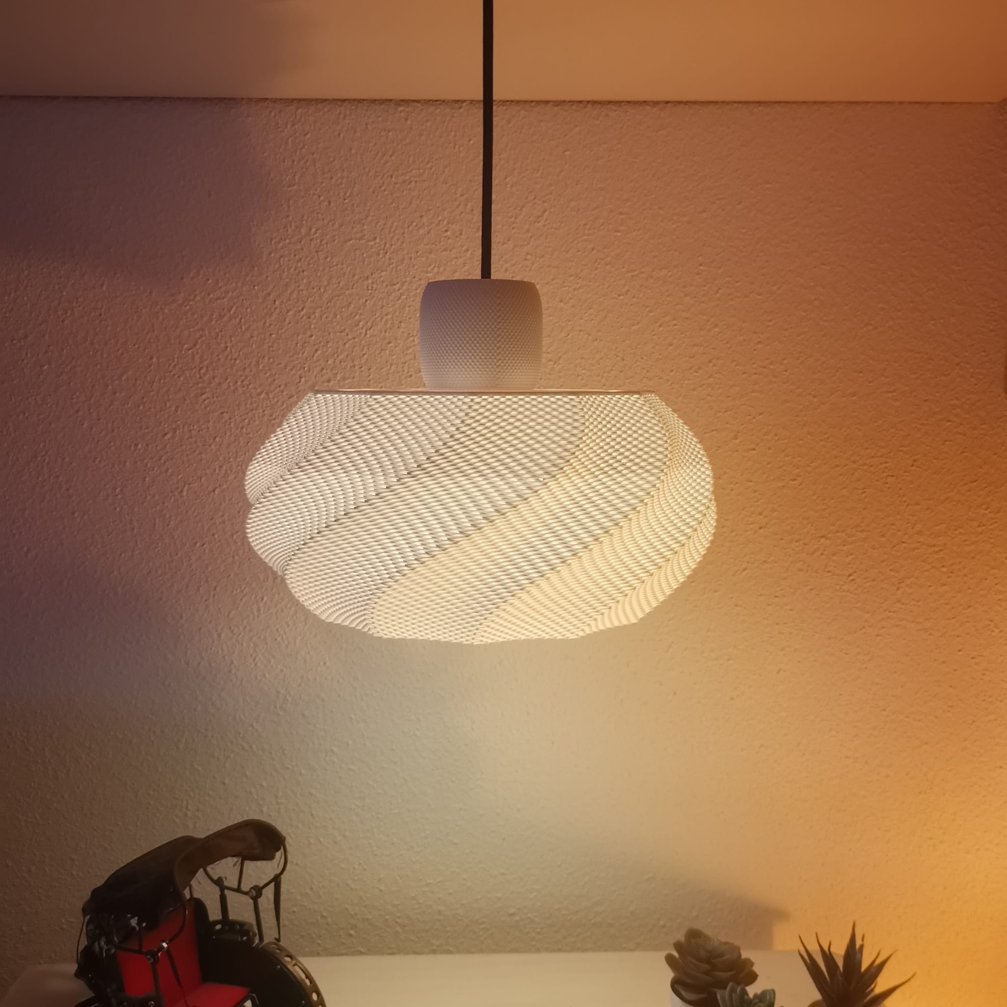 Textured pendant light fixture on a neutral wall with decorative items below.