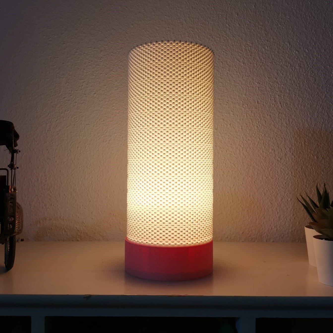 Cylindrical lamp with textured design and red base on a surface.