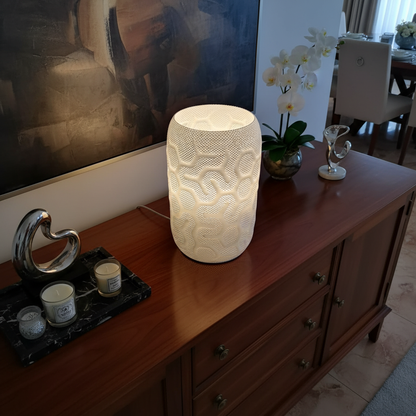 Decorative lamp on a wooden sideboard with a painting and other items in the background.