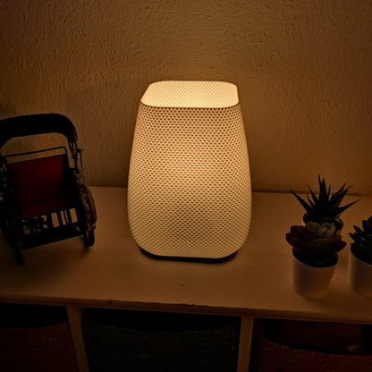 Modern textured lamp glowing softly on shelf beside decorative rickshaw and small potted succulents, warm minimalist home lighting.