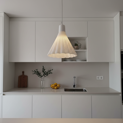 White woven pendant lamp suspended above a minimalist kitchen countertop with white cabinetry and modern decor.