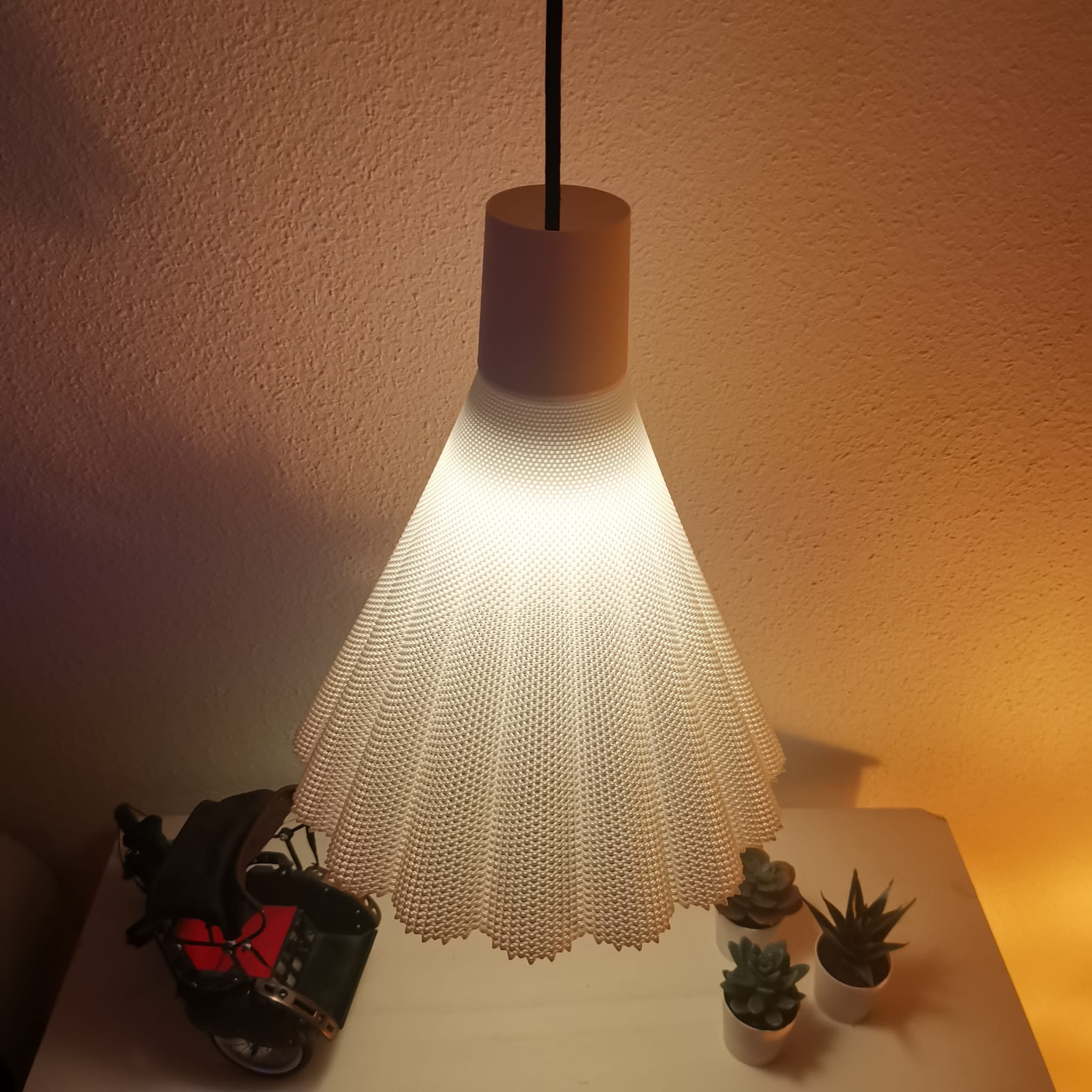 Modern pendant light with a textured shade on a table against a wall.