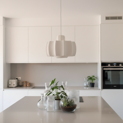 Minimalist white pendant lamp hanging above a kitchen island in a bright, modern kitchen.