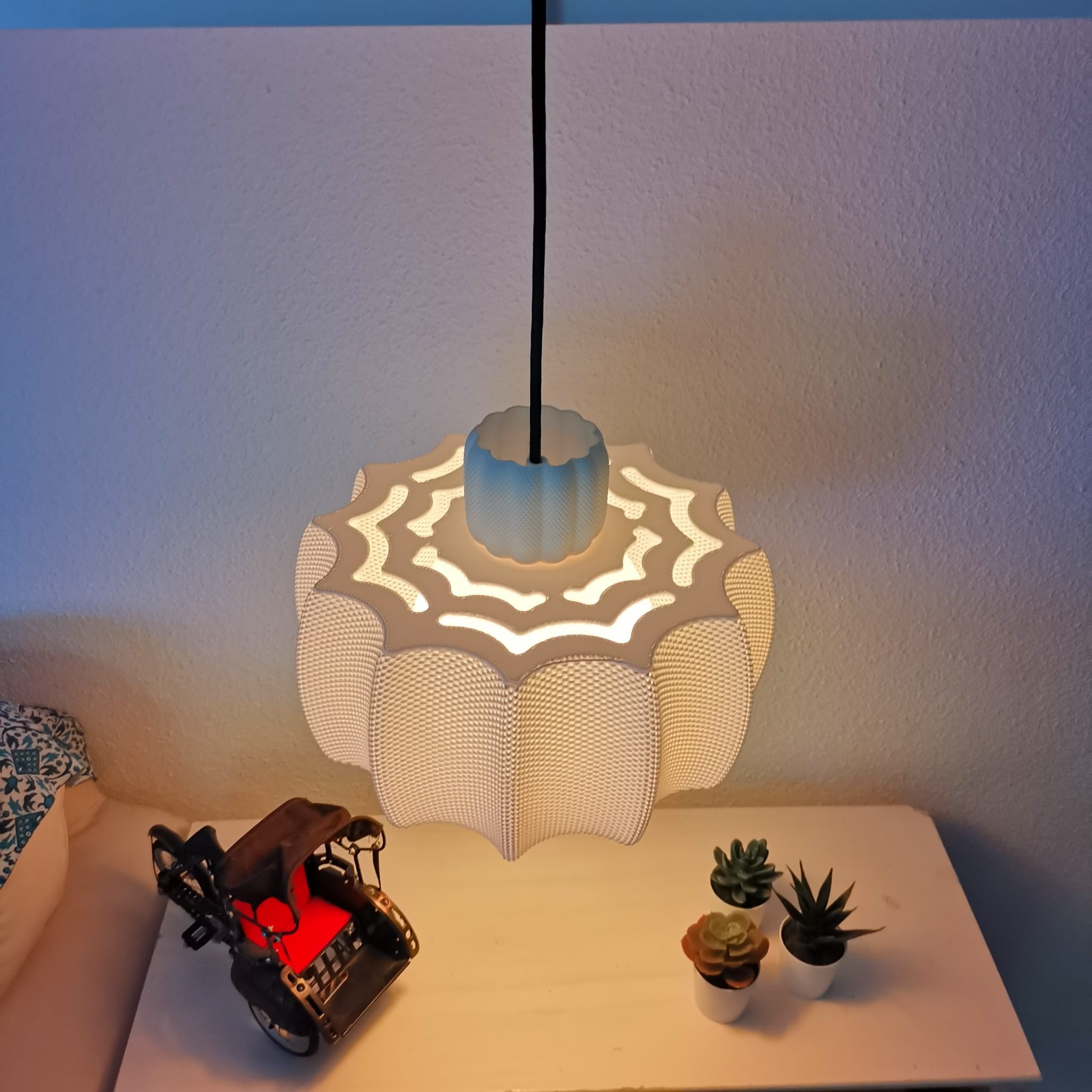 Decorative lamp with a wavy design on a table next to small plants and a toy car.