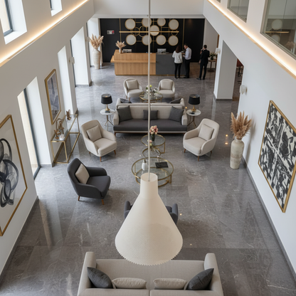 White cone-shaped pendant light hanging in a large modern hotel lobby with seating area and reception desk below.