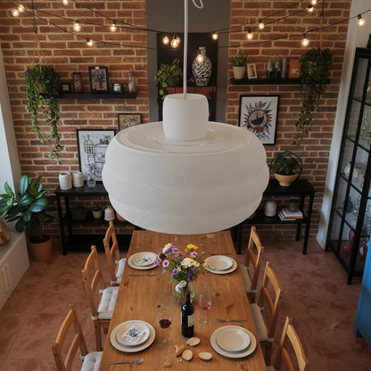 Large sculptural pendant lamp above a wooden dining table in a cozy brick-wall interior.