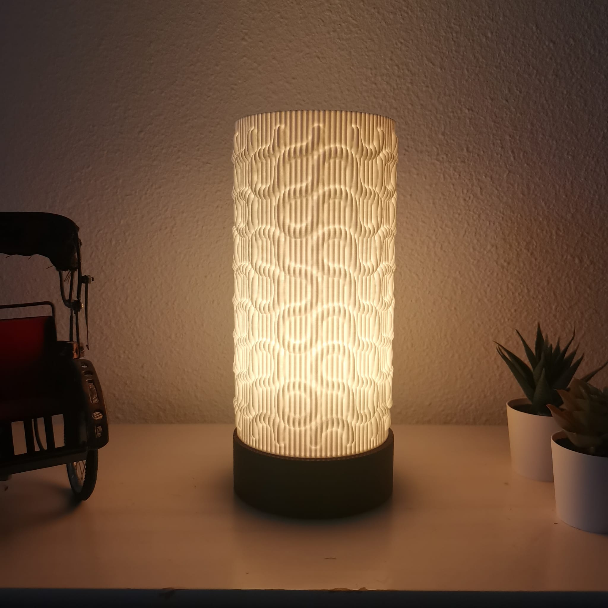 Decorative lamp with wavy pattern on a table next to a toy car and plants.