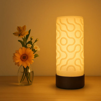 Decorative lamp with wavy pattern next to a vase of flowers on a wooden surface.