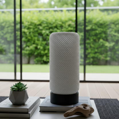 White textured lamp on a table with a plant and books in a room with large windows.