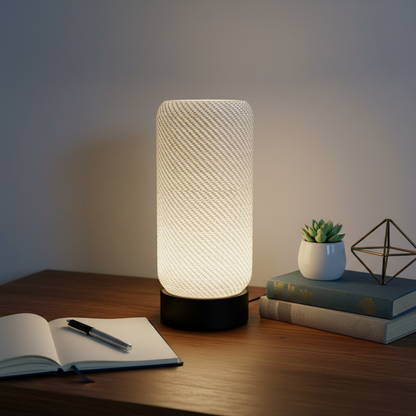 Cylindrical table lamp on a wooden surface with books and a plant