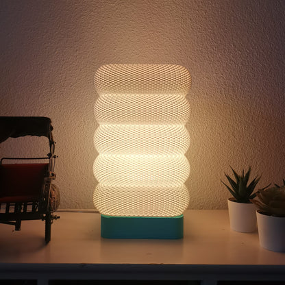 Decorative lamp with ribbed design on a table next to small plants and a model car.