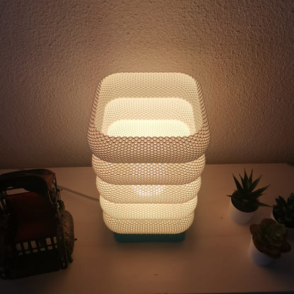 Decorative lamp with textured design on a surface with plants and a basket.