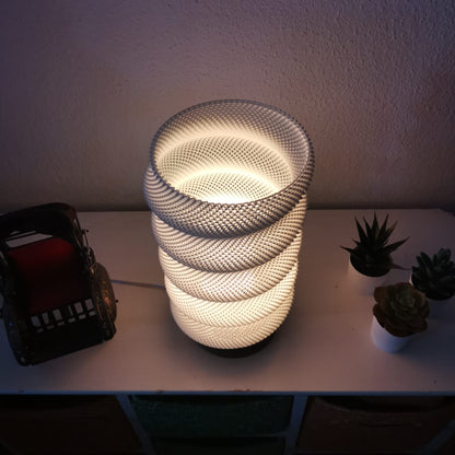 Decorative lamp with woven design on a table with plants and a small vehicle.