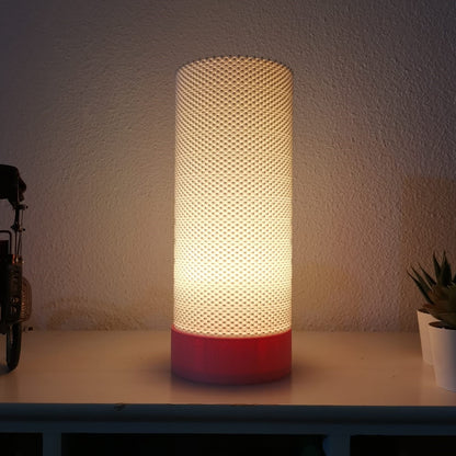 Cylindrical lamp with textured design and red base on a surface.