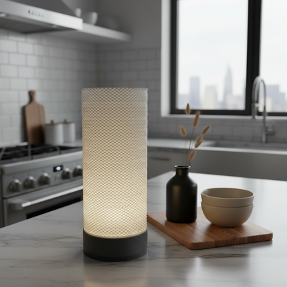 Textured cylindrical lamp on a kitchen counter with a cityscape view through a window.